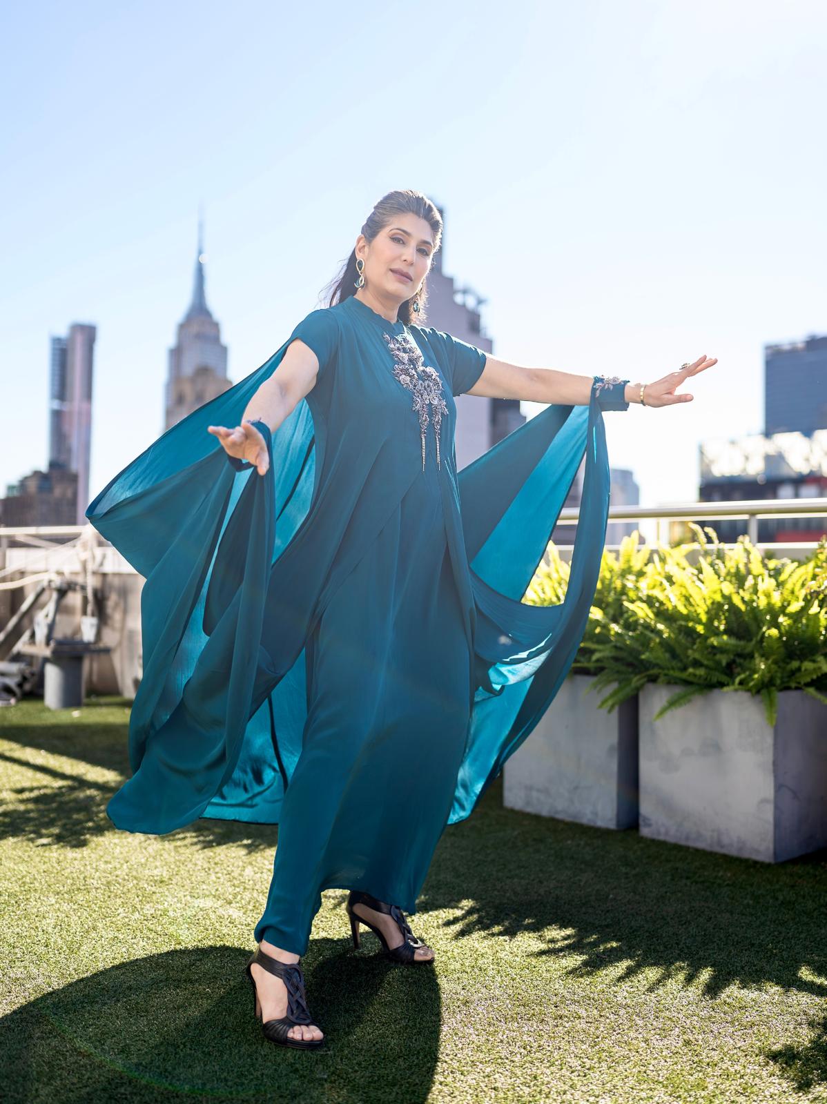 Woman in a Posh Pari teal dress with a long train on a nyc rooftop with cityscape in the background