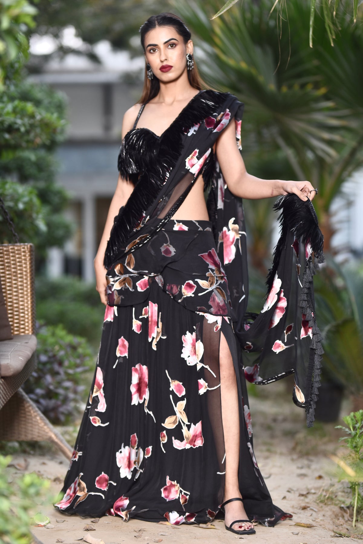 A woman wearing a black floral and feathered lengha/sari combo set with a high one-leg slit and feather details on the dupatta and blouse.