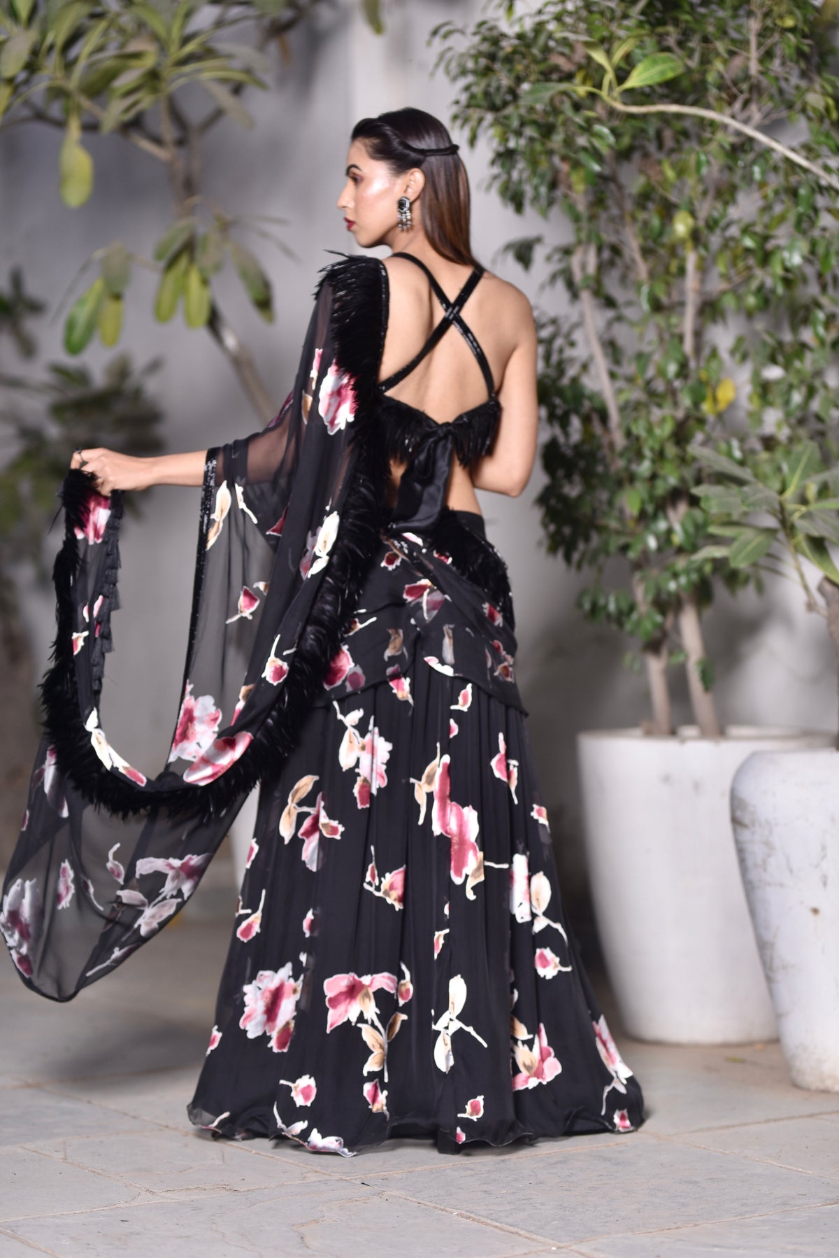 A woman wearing a black floral and feathered lengha/sari combo set with a high one-leg slit and feather details on the dupatta and blouse.