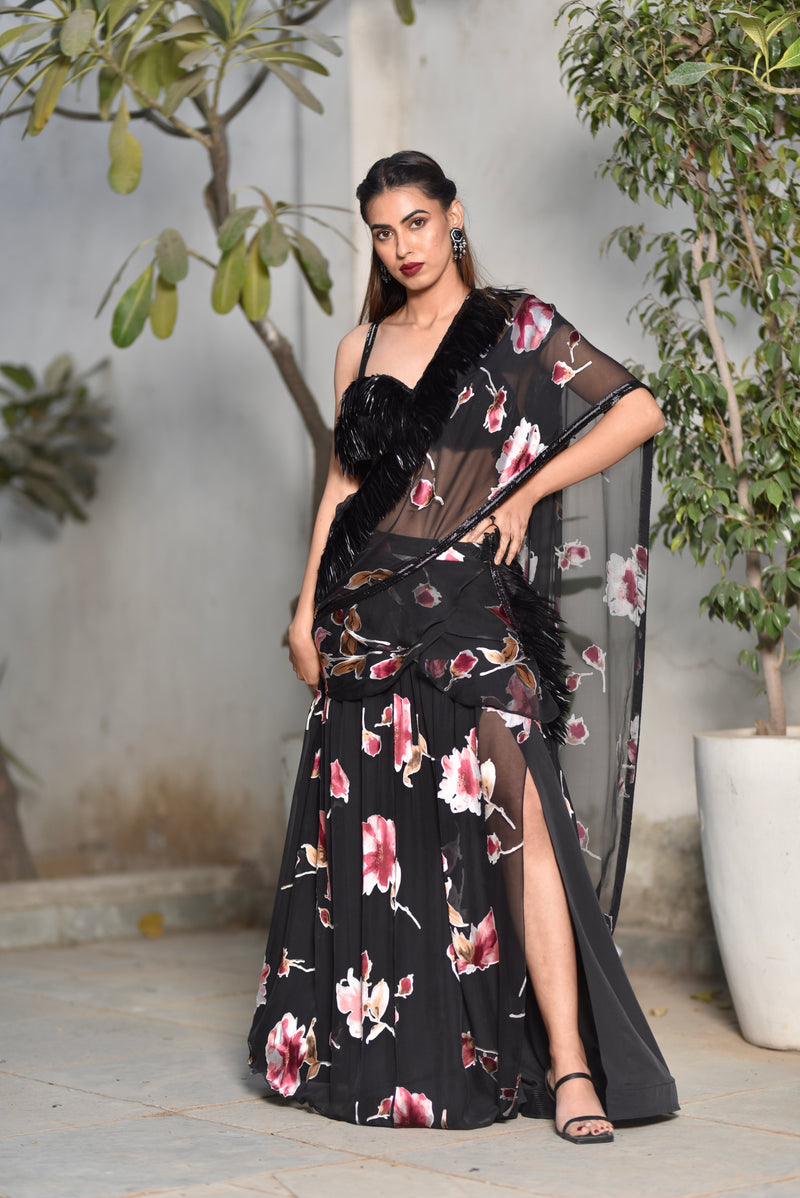 A woman wearing a black floral and feathered lengha/sari combo set with a high one-leg slit and feather details on the dupatta and blouse.