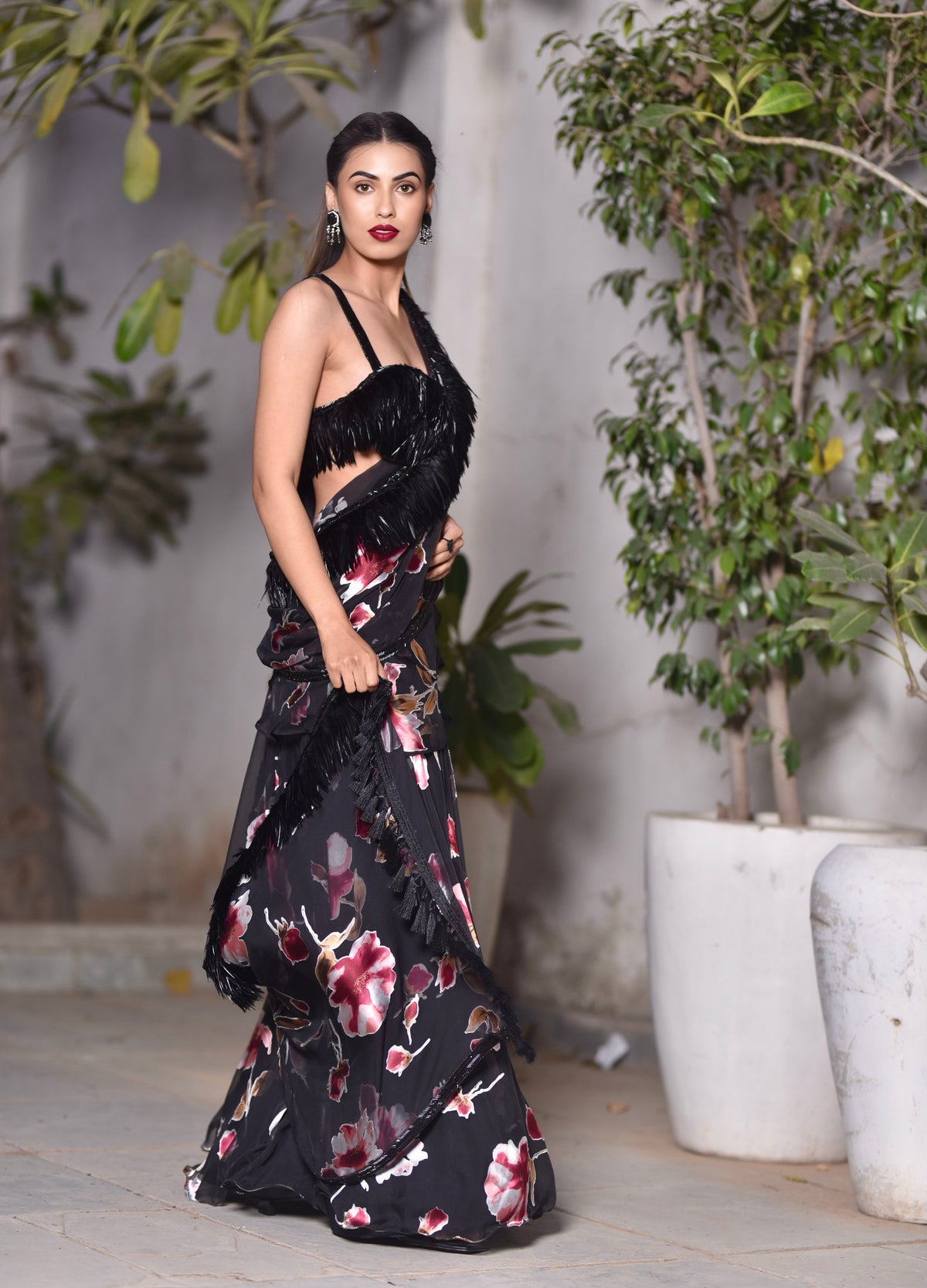 A woman wearing a black floral and feathered lengha/sari combo set with a high one-leg slit and feather details on the dupatta and blouse.