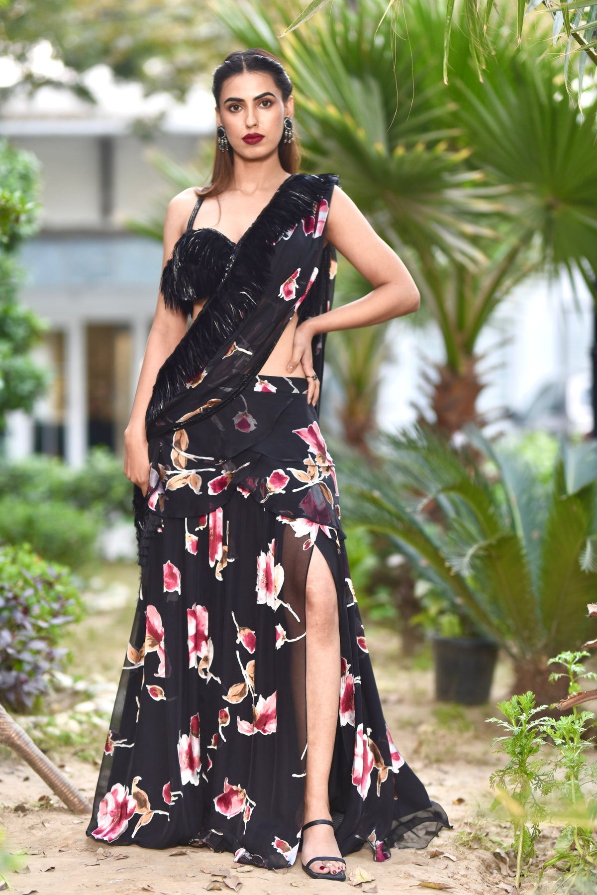 A woman wearing a black floral and feathered lengha/sari combo set with a high one-leg slit and feather details on the dupatta and blouse.