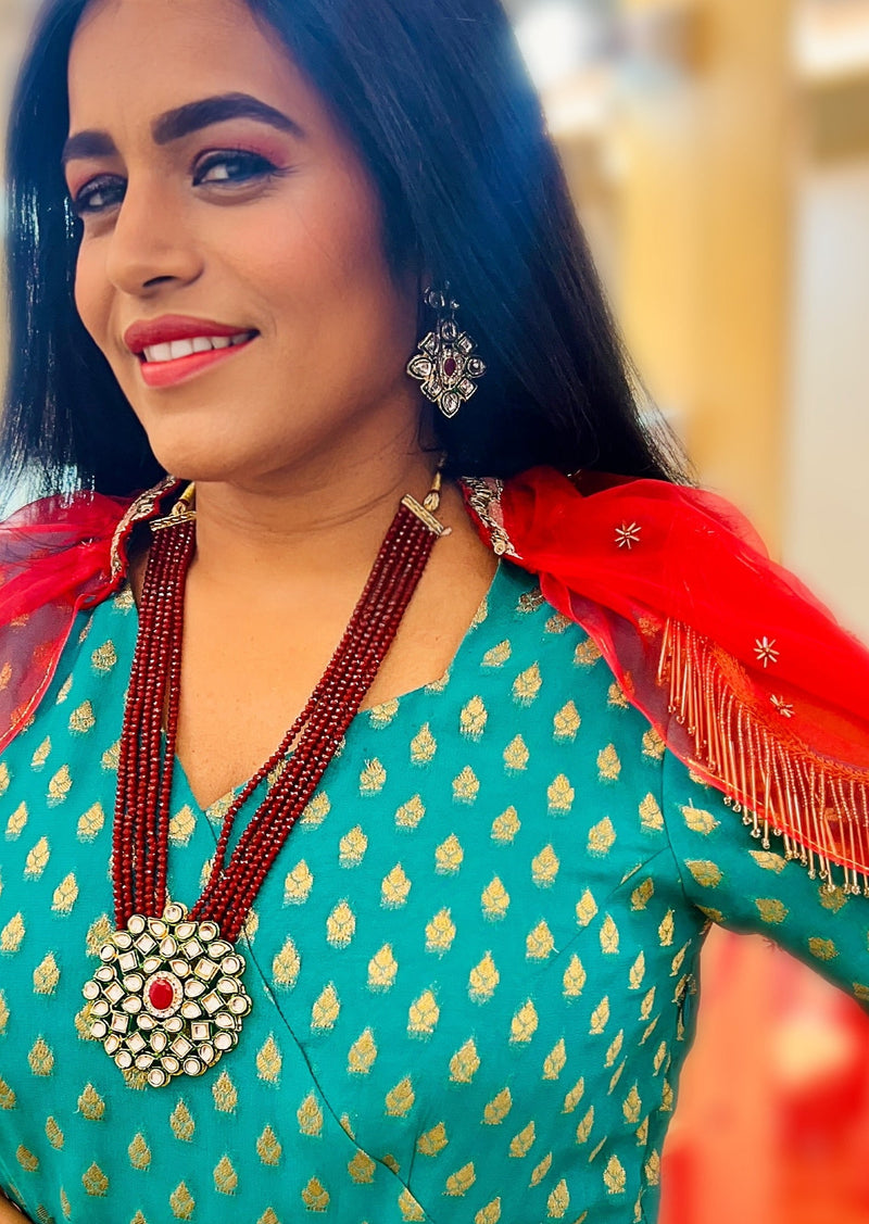 A woman wearing a green traditional outfit accessorized with a multistring red and white beaded Posh Pari necklace with a kundan motif pendant.
