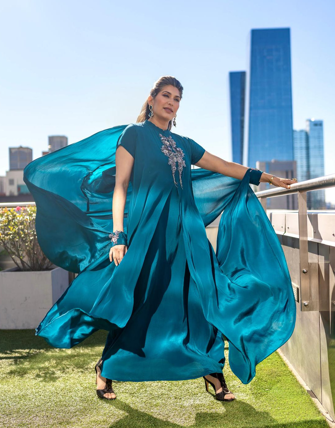Woman in a Posh Pari blue dress standing on a NyC rooftop with skyscrapers in the background